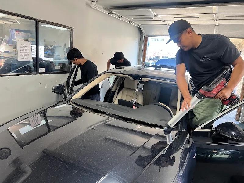 Three HV Auto Glass technicians removing a windshield from a vehicle in the shop bay